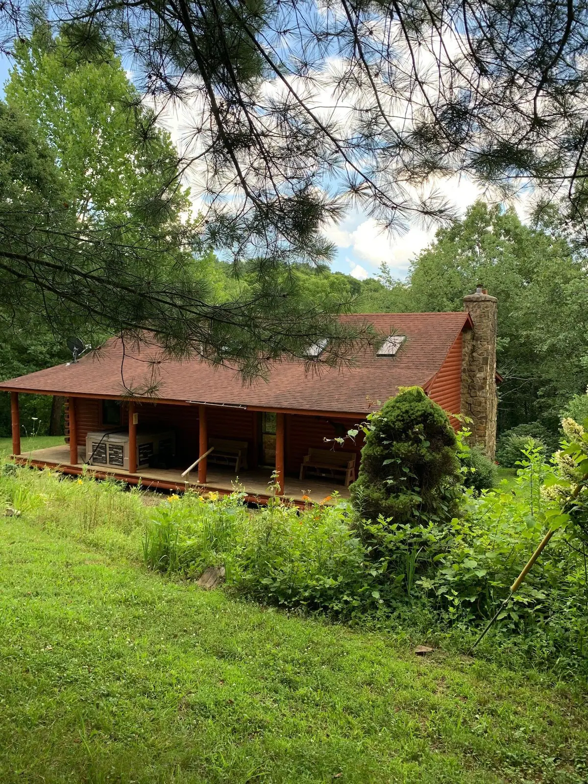 The log cabin with its stone chimney and covered front porch, framed by pine branches.