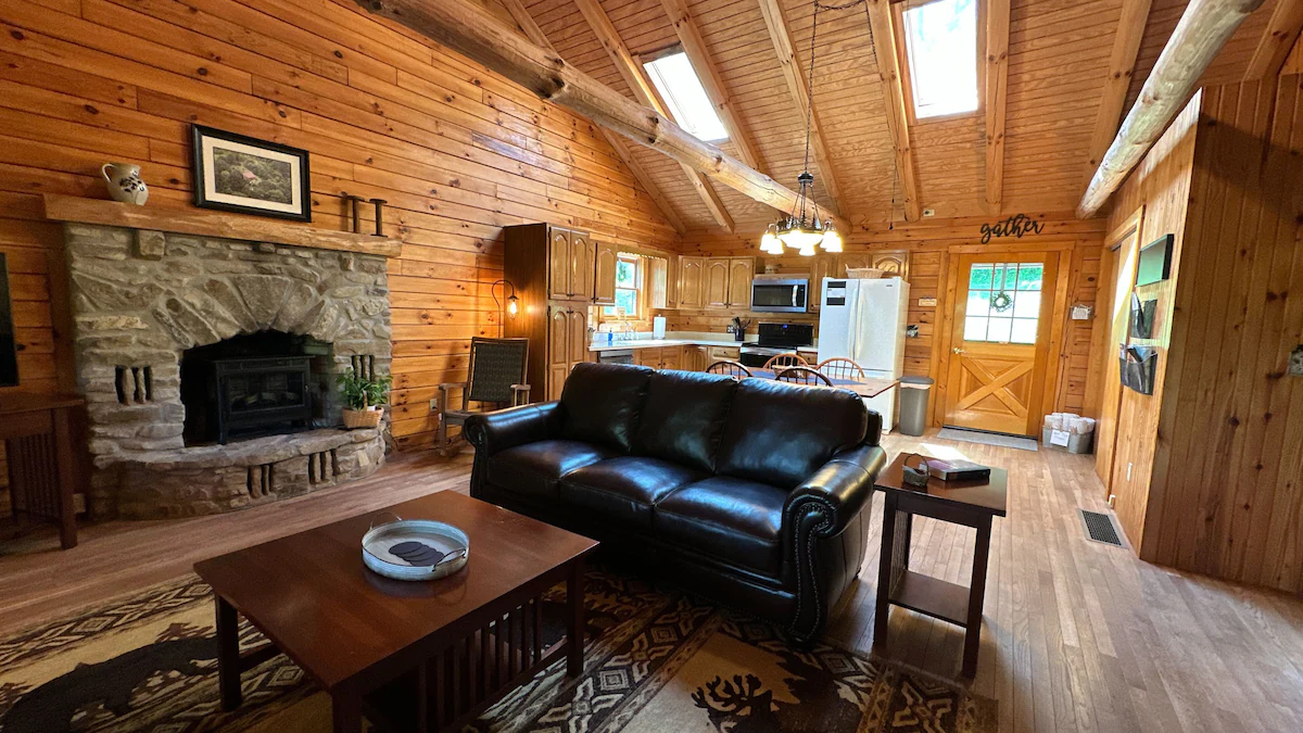 Living room with stone fireplace, leather sofa and log walls, open to the kitchen.